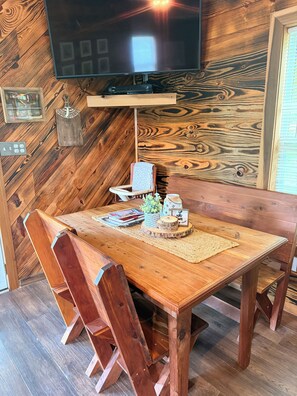 Une table à manger en bois avec des chaises, un téléviseur fixé au mur et un plancher en bois.