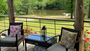Eine Holzterrasse mit Korbstühlen und einem Tisch, mit Blick auf einen See und üppiges Grün.