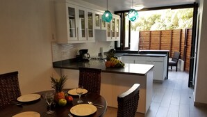 A modern kitchen with white cabinets, a central island with fruit, and a dining area with wicker chairs. - Beach front condo! Best spot to kite!! Beach lovers paradise! Nanny Estates.! (Cabarete)