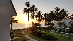 A resort with a pathway leading to the beach, palm trees, and a view of the sunset over the ocean. - Beach front condo! Best spot to kite!! Beach lovers paradise! Nanny Estates.! (Cabarete)