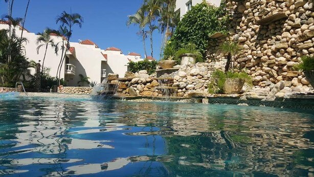 A swimming pool with clear water, surrounded by a rocky landscape and palm trees. - Beach front condo! Best spot to kite!! Beach lovers paradise! Nanny Estates.! (Cabarete)