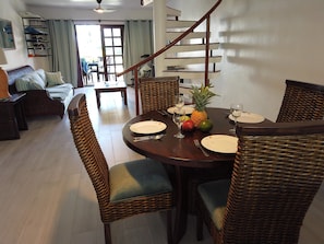Un coin repas avec des chaises en osier, une table ronde dressée pour quatre personnes et un escalier en arrière-plan.