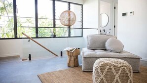 A modern living room with a large window, a round woven light fixture, a grey sofa, and a small wooden side table. - Azure Port Douglas - Luxurious & Modern Villa (Port Douglas)