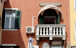 Enjoy the view from this balcony with a small window and green shutters.