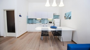 A modern kitchen with white cabinets, a microwave, and a sink. There are three chairs and a table with a blue tablecloth. - Apartment Al Porto (Rovinj)