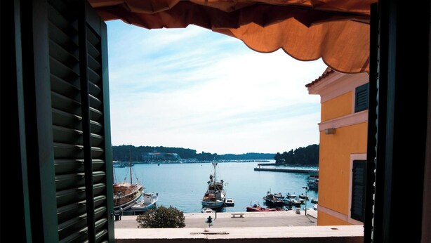 A view from a window with shutters, overlooking a harbor with boats and a distant shoreline. - Apartment Al Porto (Rovinj)
