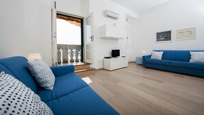 A modern living room with blue sofas, a white entertainment unit, and a balcony with a view. - Apartment Al Porto (Rovinj)