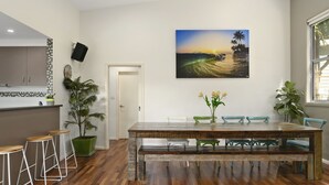Een eetgedeelte met een houten tafel, vier stoelen en een bank. Op de muur hangt een schilderij van een zonsondergang.