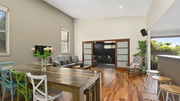 Een ruime woonkamer met een houten eettafel, groene en witte stoelen, een bank en een televisie.