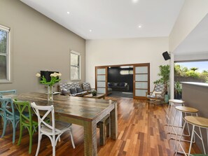 Un vaste espace de vie comprenant une table à manger en bois, des chaises vertes et blanches, un canapé et un téléviseur.