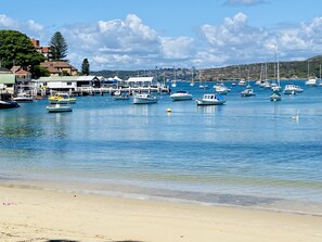 A marina with various boats docked, a sandy beach, and buildings in the background.
