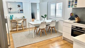 A modern kitchen with white cabinetry, a dining area with a wooden table and chairs, and a kitchen island with a sink and countertop. - Manly Beach Retreat in walkable great location, with bonus rare onsite parking (Manly)