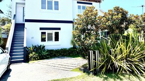 A two-story house with a staircase leading to the entrance, a driveway, and a well-maintained garden with various plants. - Manly Beach Retreat in walkable great location, with bonus rare onsite parking (Manly)
