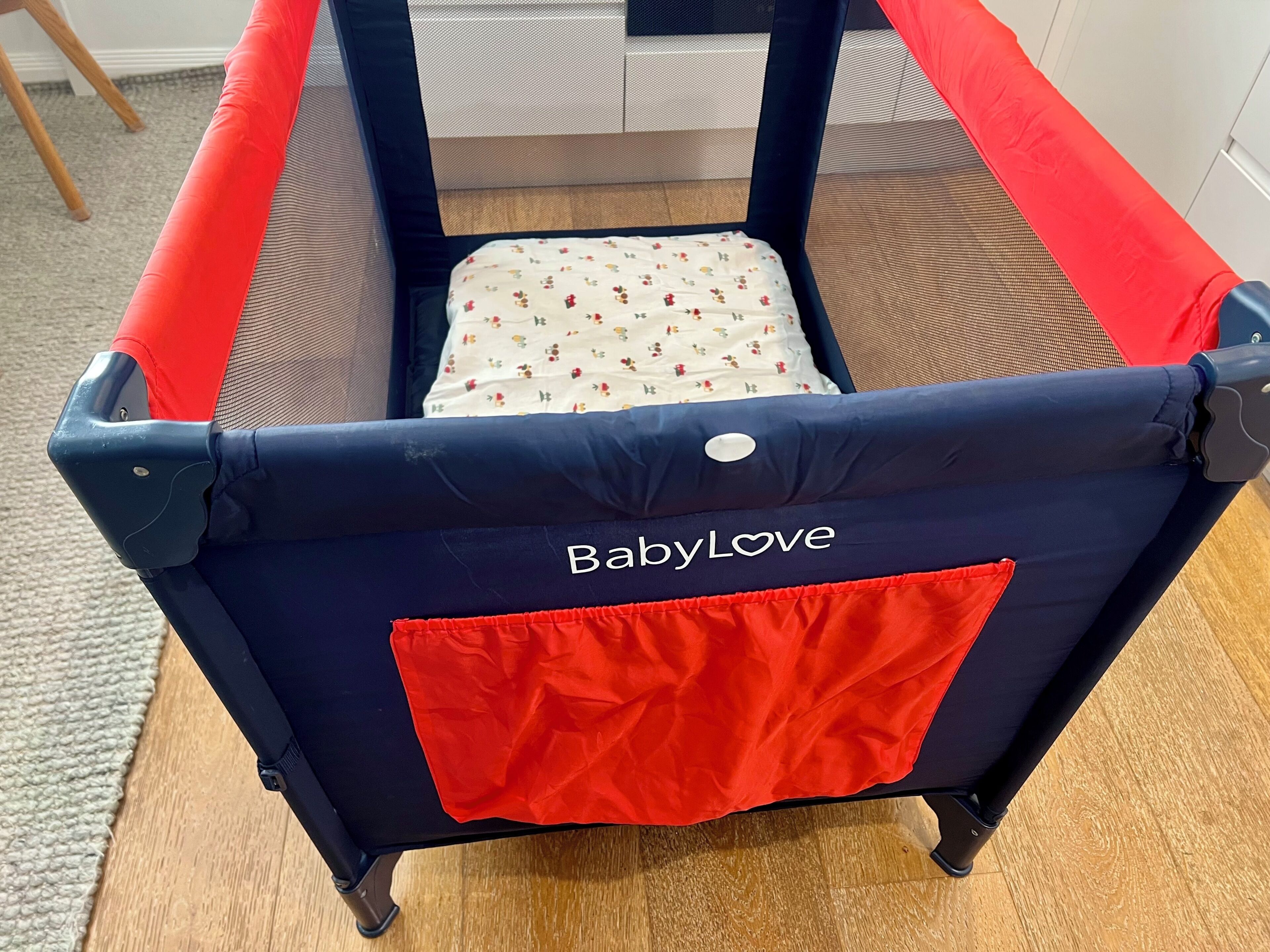 A baby playpen with a mesh top, a red cushion, and the brand name 'BabyLove' on the back.