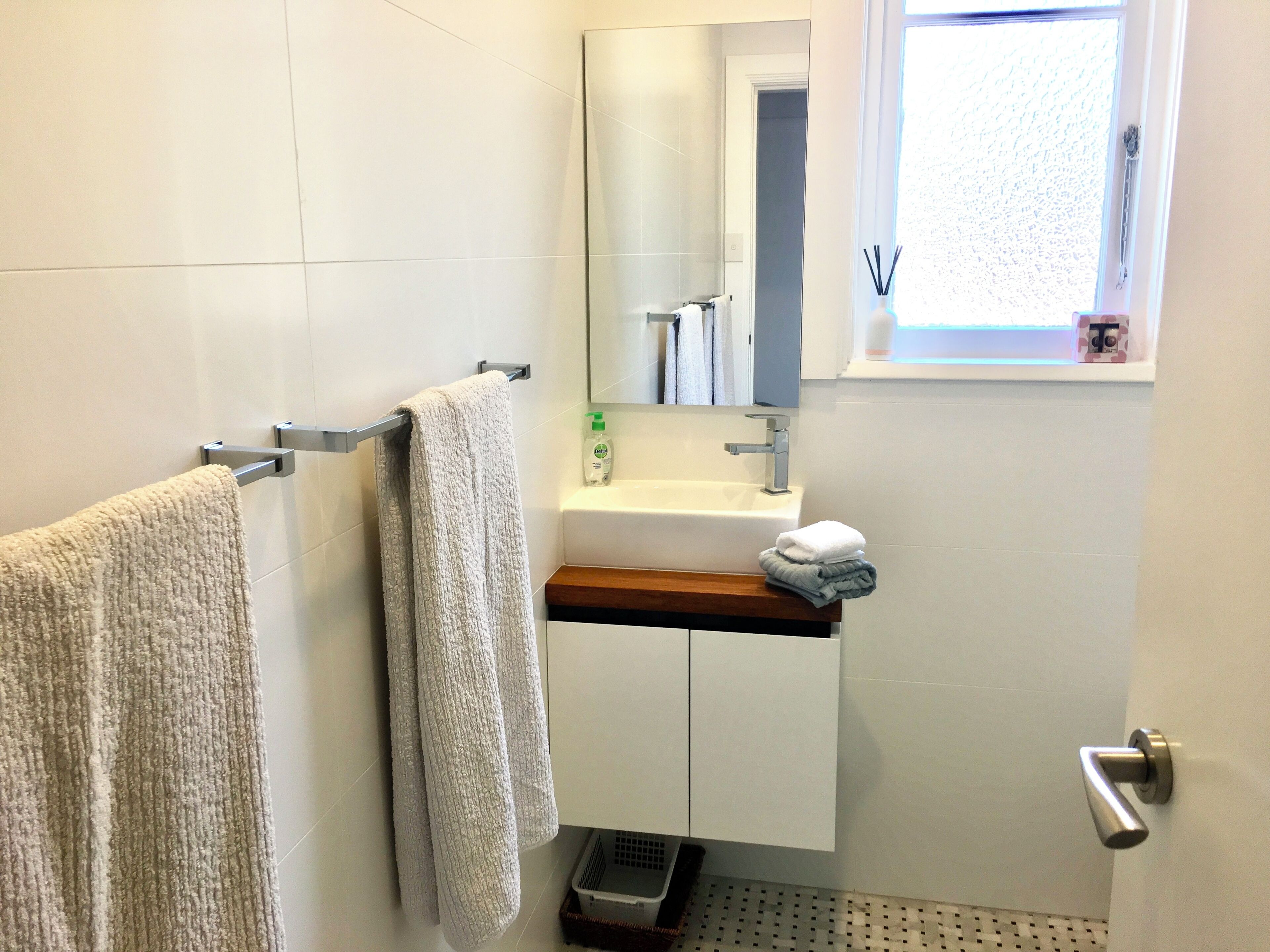 A bathroom with a towel rack, a sink, a mirror, and a window.