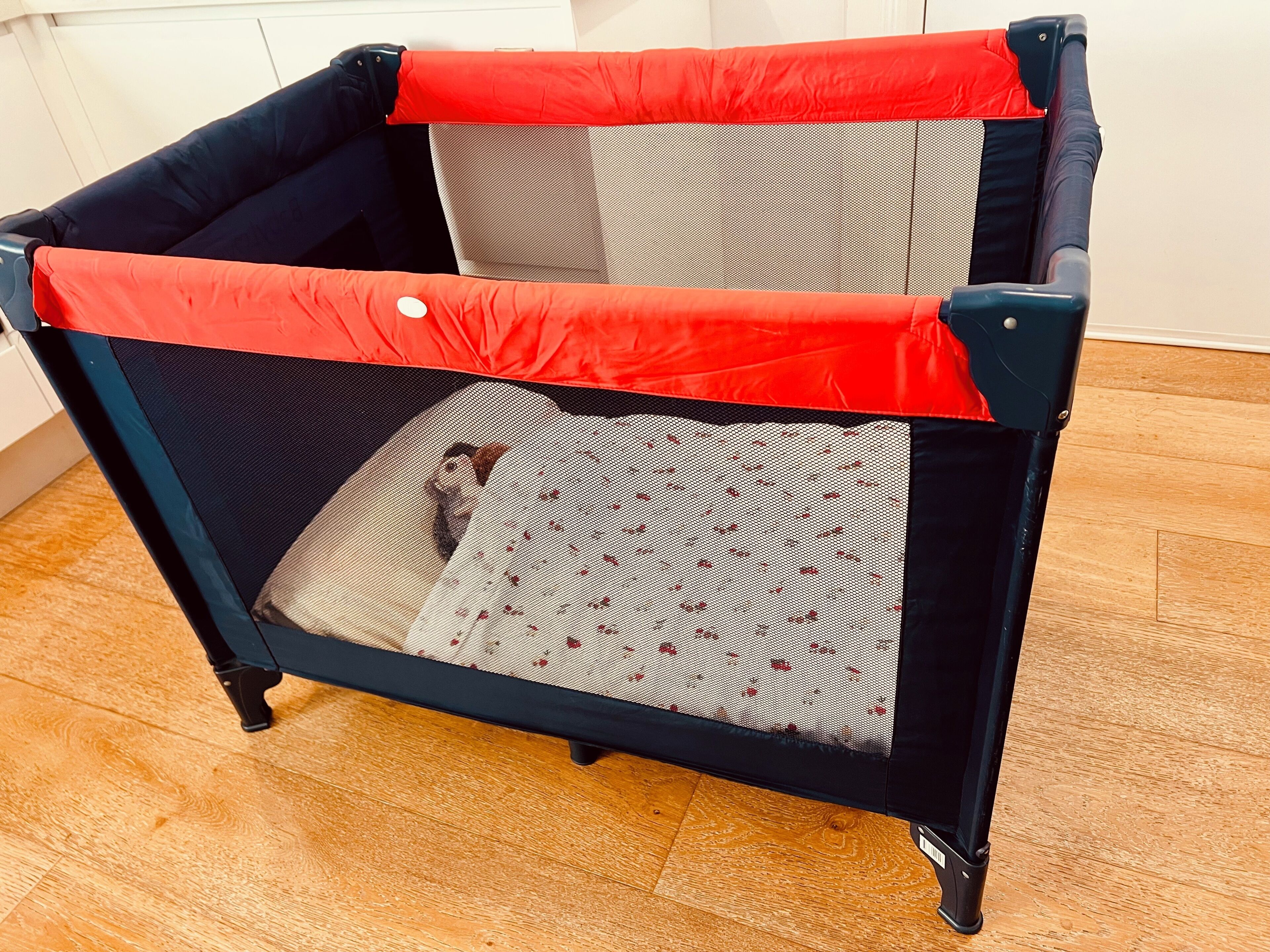 A black and red baby playpen with a mesh backrest and a solid floor.