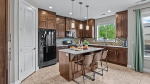 Cocina moderna con armarios de madera, un refrigerador negro, una isla central con taburetes altos e iluminación colgante.