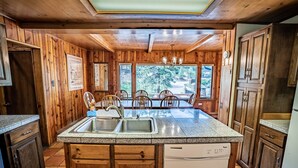 Una cocina con armarios de madera, encimeras de granito, lavavajillas y un comedor con sillas y una mesa.