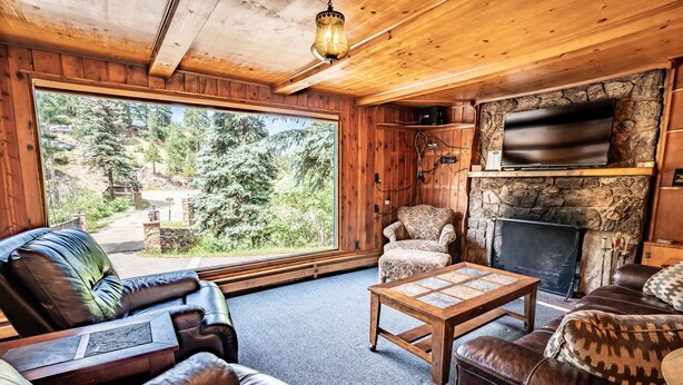 Interior acogedor de una cabaña con chimenea de piedra, sofás de cuero y un amplio ventanal con vistas al bosque.