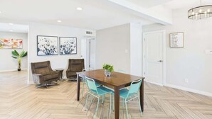 A spacious room with a wooden herringbone floor, a dining table with chairs, a sofa, and a potted plant.