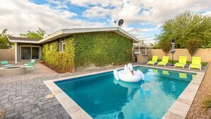 A swimming pool with a swan float, green chairs, and a building with a green wall.