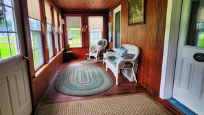 Een houten interieur met een schommelstoel, een fauteuil en een kamerkleed met patroon.