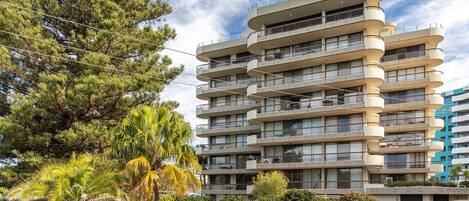 A multi-story residential building with balconies, surrounded by trees and greenery.