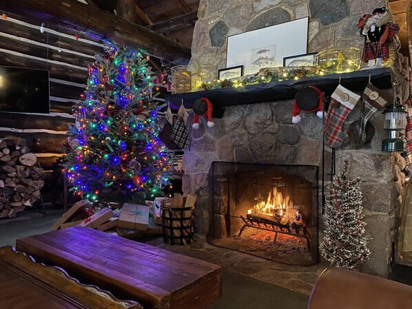 Ein gemütliches Zimmer mit Kamin aus Stein, einem Weihnachtsbaum und einer hölzernen Bank.