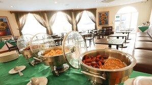 A buffet setup with various food items in metal containers, a green tablecloth, and a seating area with tables and chairs. - Hotel Mansion Teodolinda (Managua)