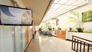 A hotel corridor with a sign indicating the ENACAL restaurant hours, wooden benches, potted plants, and a tiled floor. - Hotel Mansion Teodolinda (Managua)