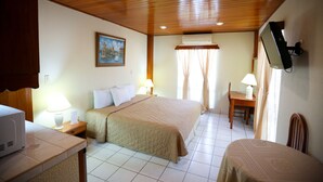 A hotel room with a wooden ceiling, a bed with a beige bedspread, a desk with a lamp, and a television mounted on the wall. - Hotel Mansion Teodolinda (Managua)