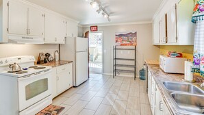 Una cucina con mobili bianchi, un fornello, un frigorifero, un lavello e un forno a microonde.