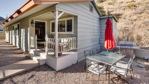 Una casa con portico coperto, barbecue e tavolo con sedie.