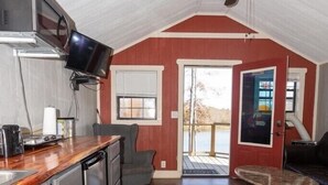 Eine kompakte Küche mit Einbauofen, Fernseher und Kaffeemaschine. Es gibt eine Essecke mit Tisch und Stühlen sowie einen Deckenventilator.