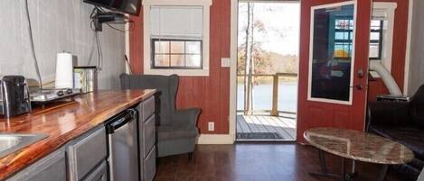 A compact kitchen with a built-in oven, a TV, and a coffee maker. There is a dining area with a table and chairs, and a ceiling fan.
