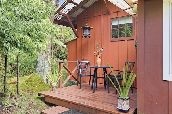 A wooden deck with a table and chairs, surrounded by potted plants and a hanging lantern.