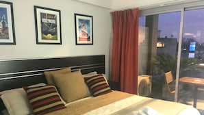 Ein Hotelzimmer mit einem großen Bett, Kissen, einem Fenster mit Vorhängen und gerahmten Postern an der Wand.