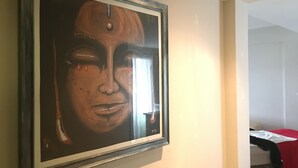 Ein gerahmtes Kunstwerk an einer Wand in einem Zimmer mit Bett und Fenster.