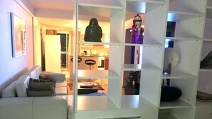 Ein Wohnzimmer mit einem weißen Sofa, einer weißen Kommode mit Schubladen und einer Küche im Hintergrund.
