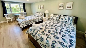 A bedroom with two beds, a small table, a chair, and a window with curtains. - Sandy Neck Motel (East Sandwich)