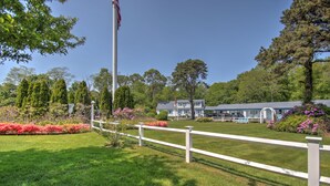 A well-maintained lawn with a white fence, a flagpole, and a building with a blue roof in the background. - Sandy Neck Motel (East Sandwich)