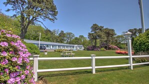 A hotel with a white fence, picnic tables, and a parking area. - Sandy Neck Motel (East Sandwich)