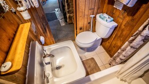 Ein Badezimmer mit Holzeinrichtung, einem weißen Waschbecken mit Chromarmatur, einer Toilette und einer kleinen Holzbank.