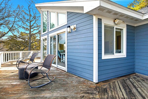 A blue house with a deck, a rocking chair, and a window.
