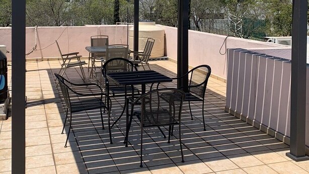 Une terrasse extérieure couverte, équipée d’une table et de chaises, d’un barbecue, et offrant une vue sur les montagnes en arrière-plan.