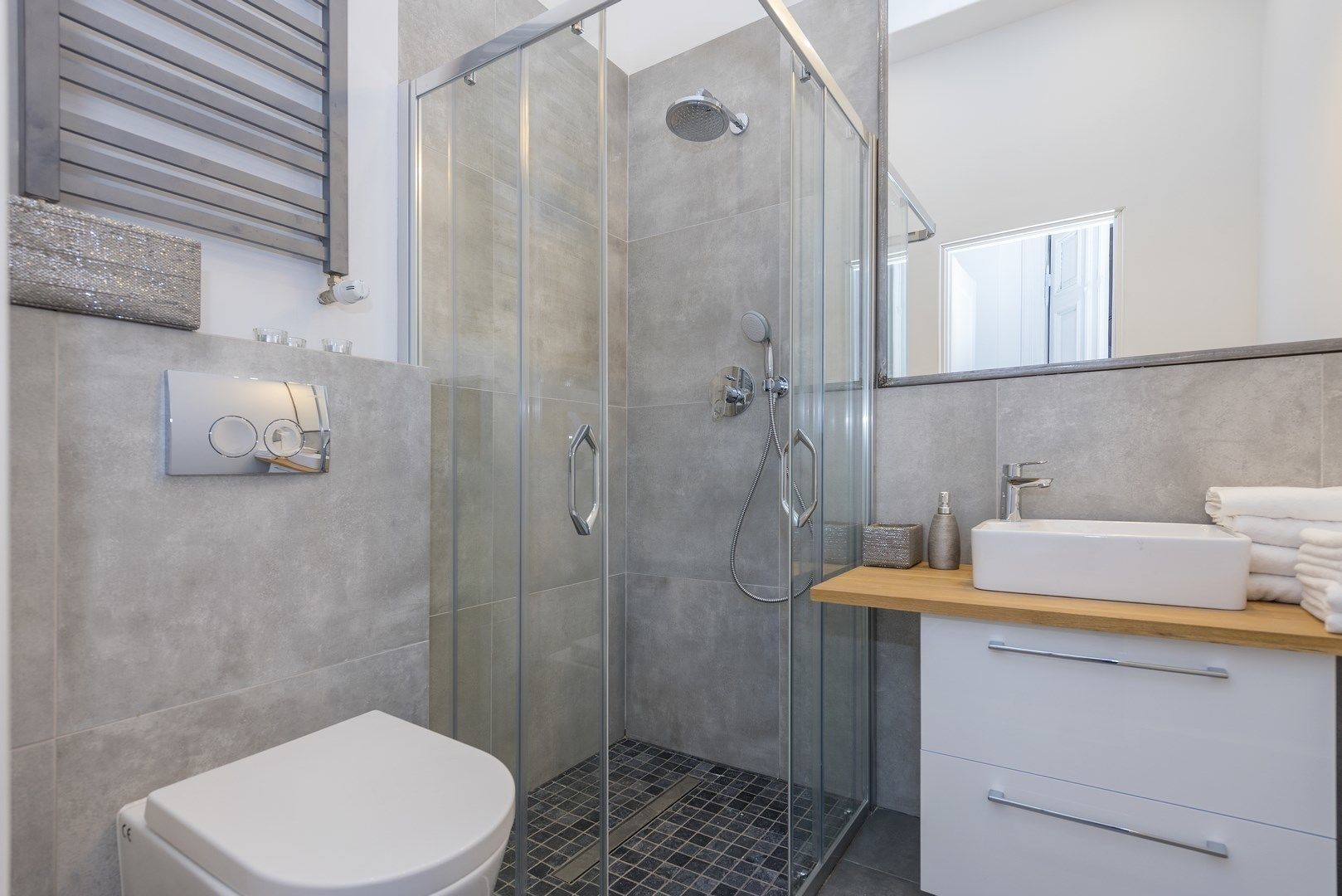 A modern bathroom with a glass-enclosed shower, a white toilet, and a vanity with a sink and towel stack.