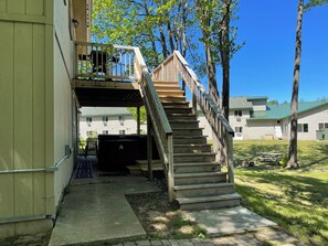 Una scala in legno conduce a una zona esterna coperta con piscina, circondata da alberi e un edificio con diverse finestre.