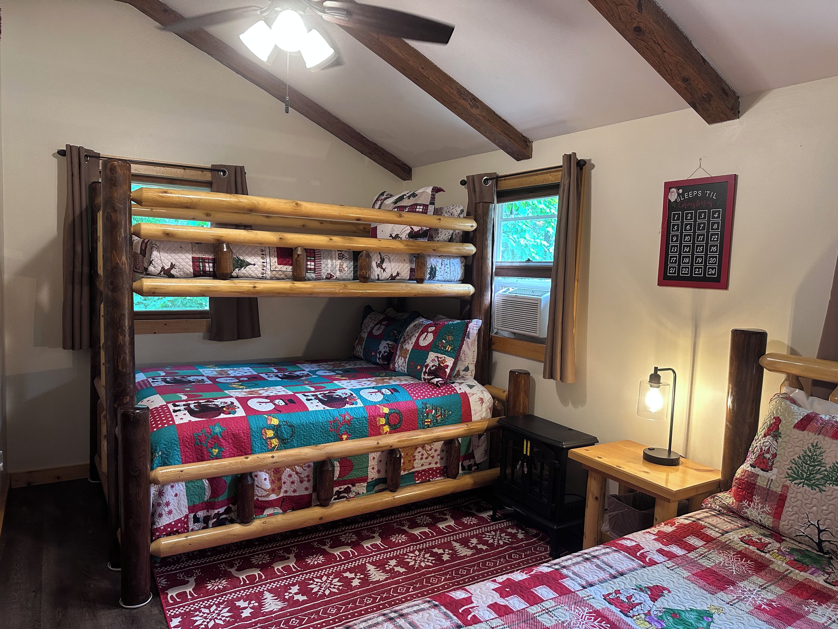 A bunk bed with a quilt, a bedside table with a lamp, and a calendar on the wall.