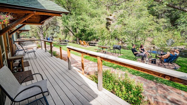 Un terrazzo in legno con posti a sedere all'aperto e un tavolo da picnic, circondato da vegetazione rigogliosa e un piccolo stagno.