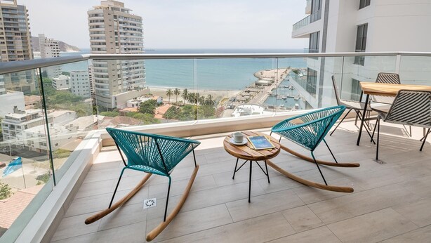 A balcony with two rocking chairs and a table, overlooking a beach and cityscape. - SUPERIOR APARTMENT, 1 BEDROOM - 70 METERS LARGE (Santa Marta)